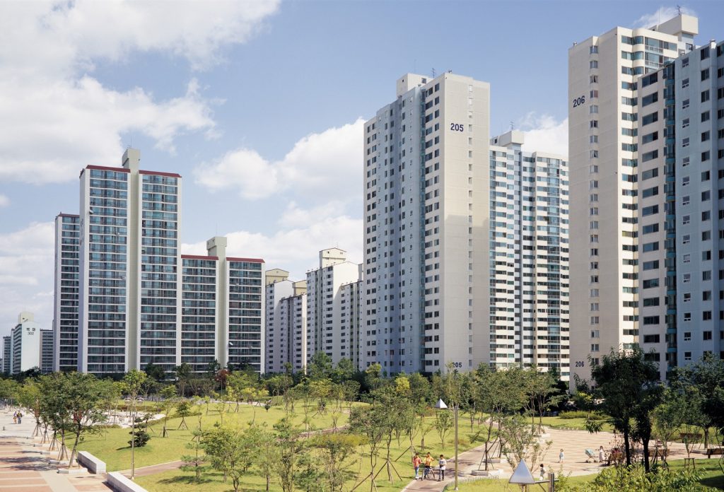 공원을 낀 고층 아파트 단지, 맑은 하늘 아래 산책로와 잔디밭